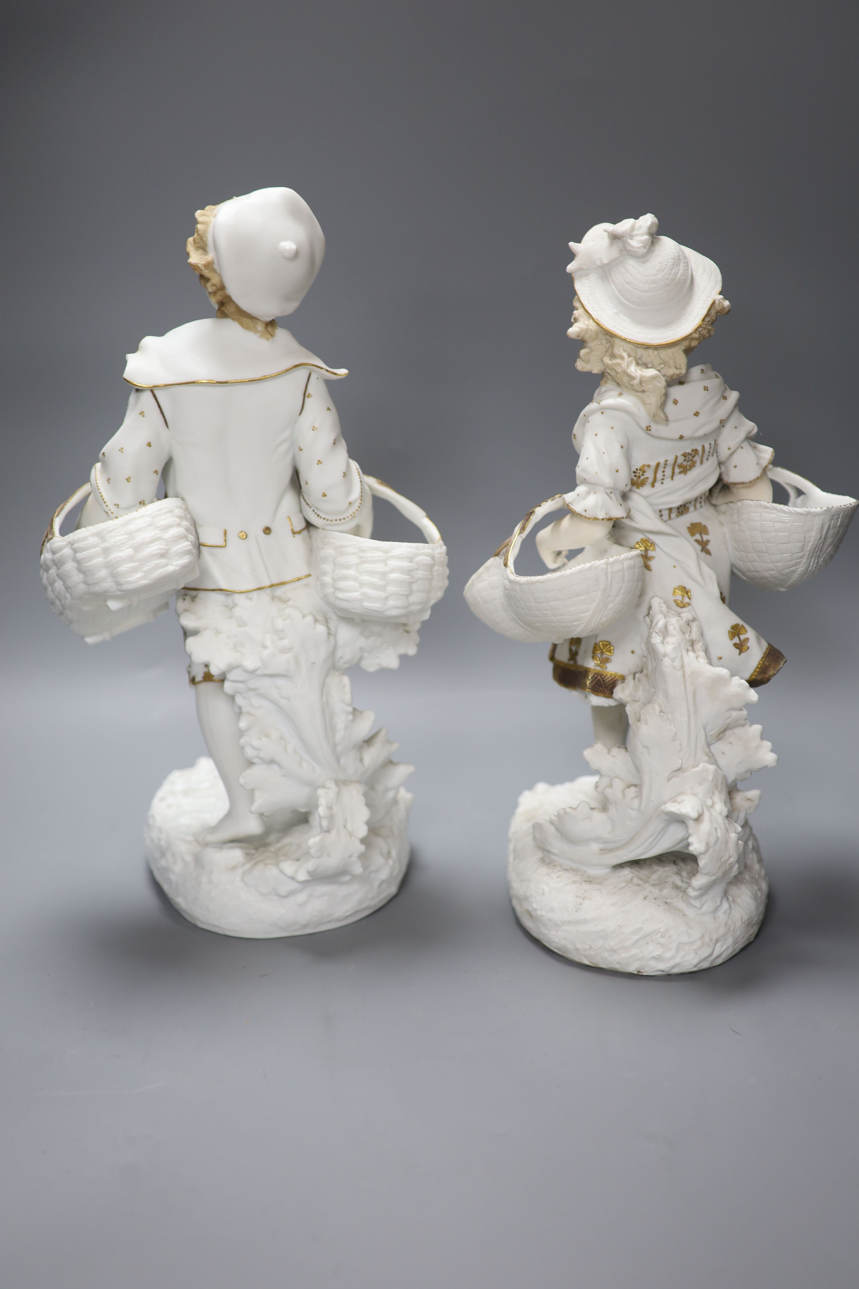 A pair of 19th century bisque gilt painted and decorated figures of a peasant boy and girl carrying baskets, 36cm
